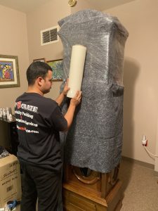 Ship-n-Crate packer shrink-wrapping a blanket-padded antique grandfather clock for long-distance shipping